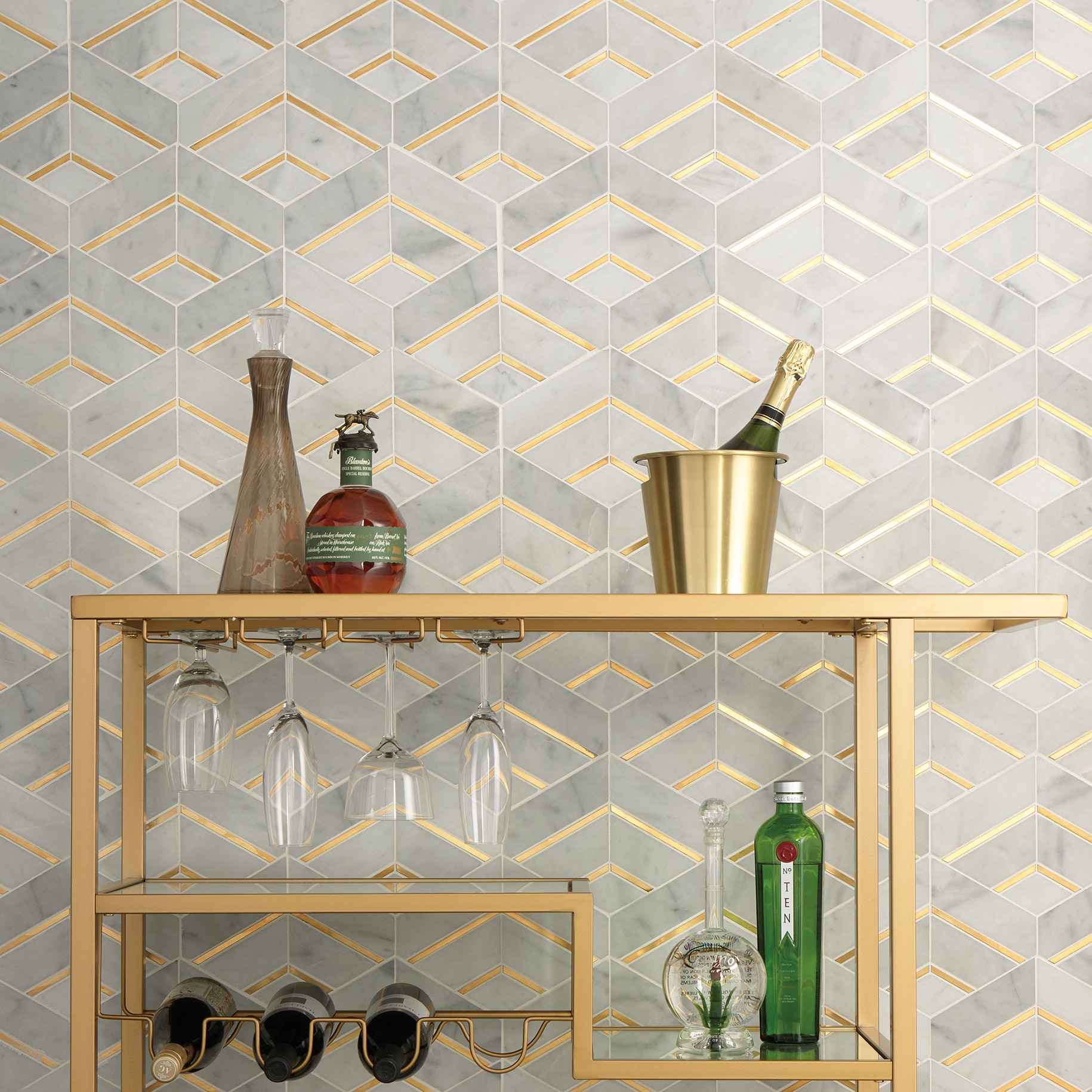 Wet bar with bookmatched marble-and-brass tile wall, gold bar cart, and glassware