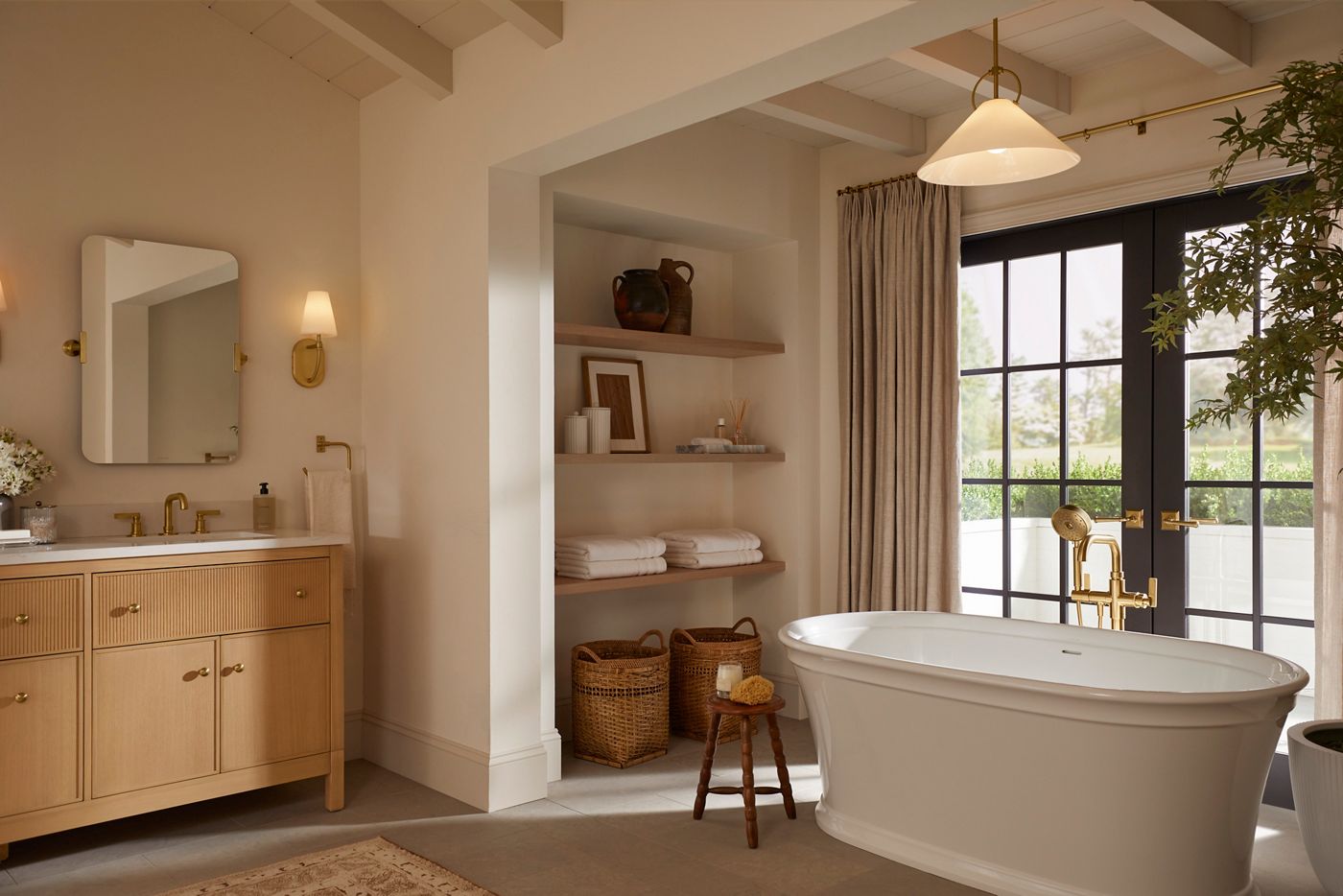 Warm, naturally lit bathroom with a wood vanity, brass fixtures, and freestanding tub